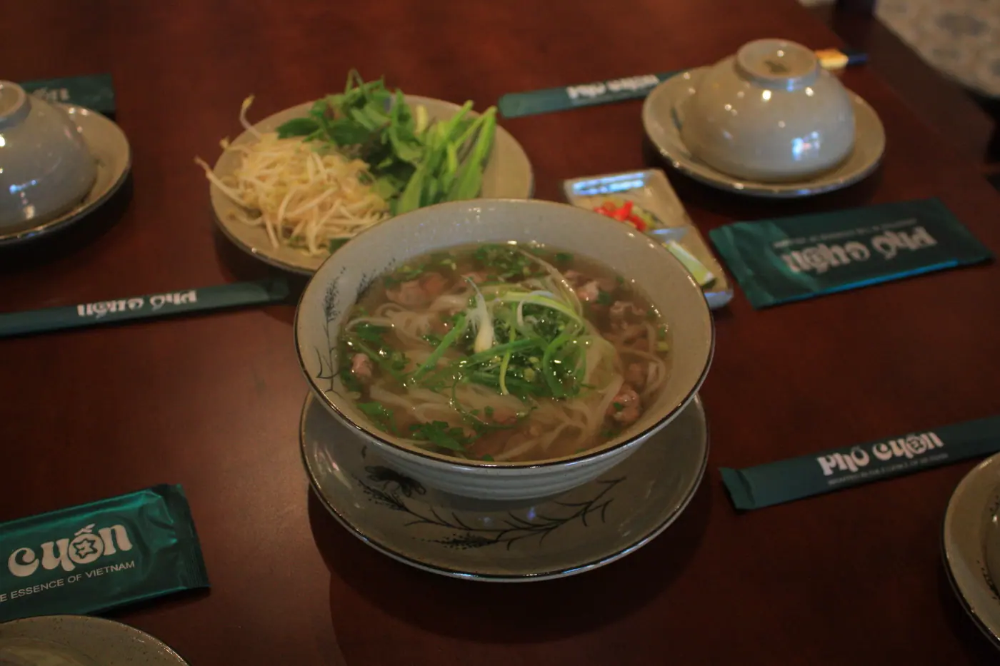 Tô phở bò kèm giá đỗ và rau thơm trên bàn ăn