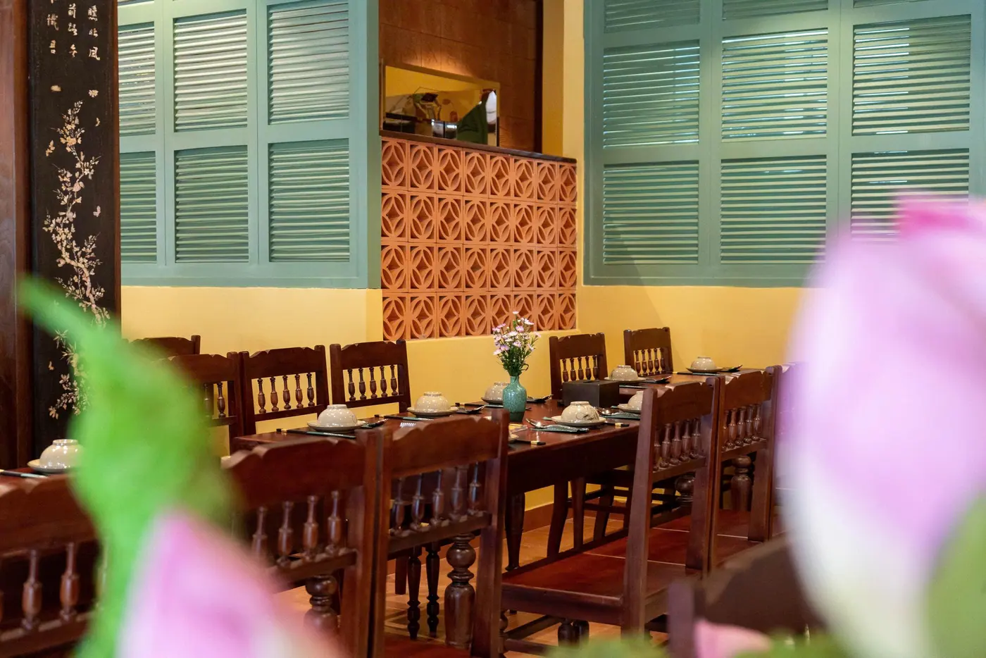 Phòng ăn với bàn gỗ được set sẵn nhìn qua khung hoa